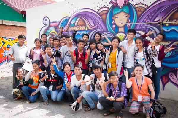 Students posing in front of a street art mural in a Phnom Penh street