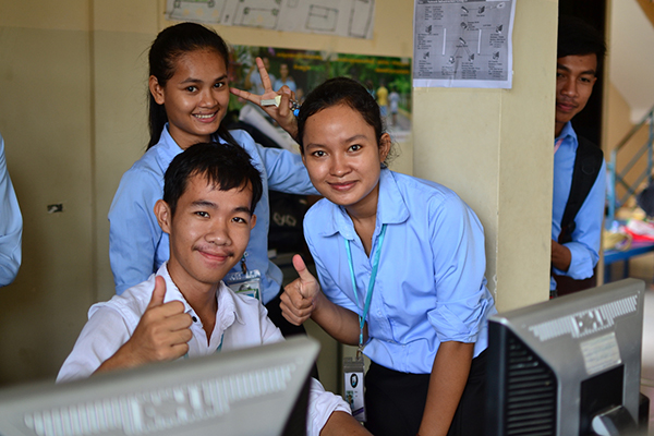 Etudiants, deux filles et un garçon, joyeux devant des ordinateurs